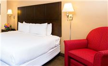 A hotel room with a large bed, red armchair, and wall lamps.