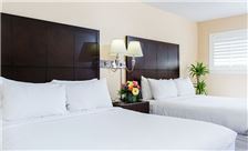 A hotel room with two double beds, nightstand, and plant.