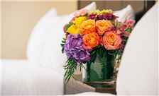 A vase of colorful flowers on a bed with white pillows.