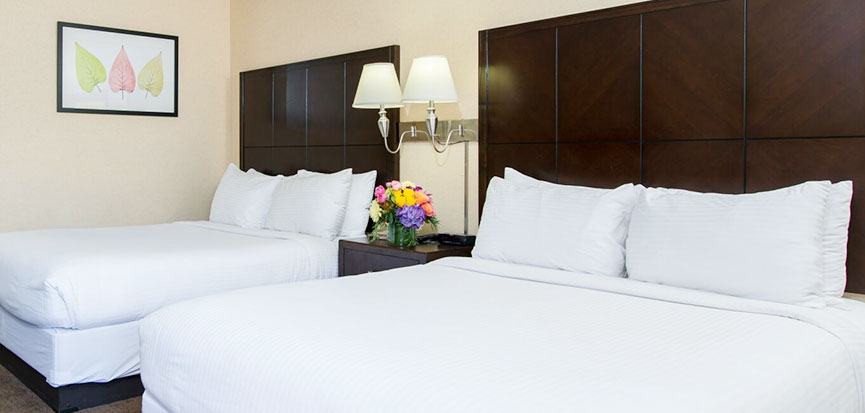 A hotel room with two double beds, a nightstand with a lamp and flowers, and a framed picture on the wall.