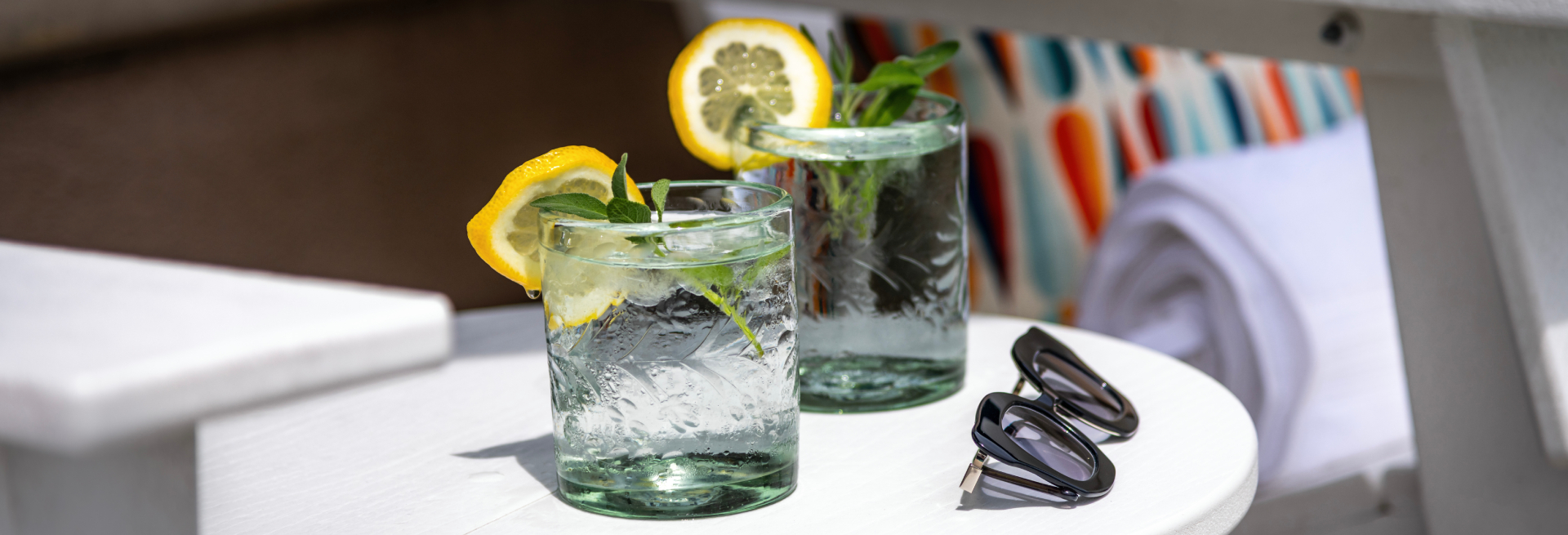 Two glasses of lemonade with mint and lemon slices on a white table with sunglasses.